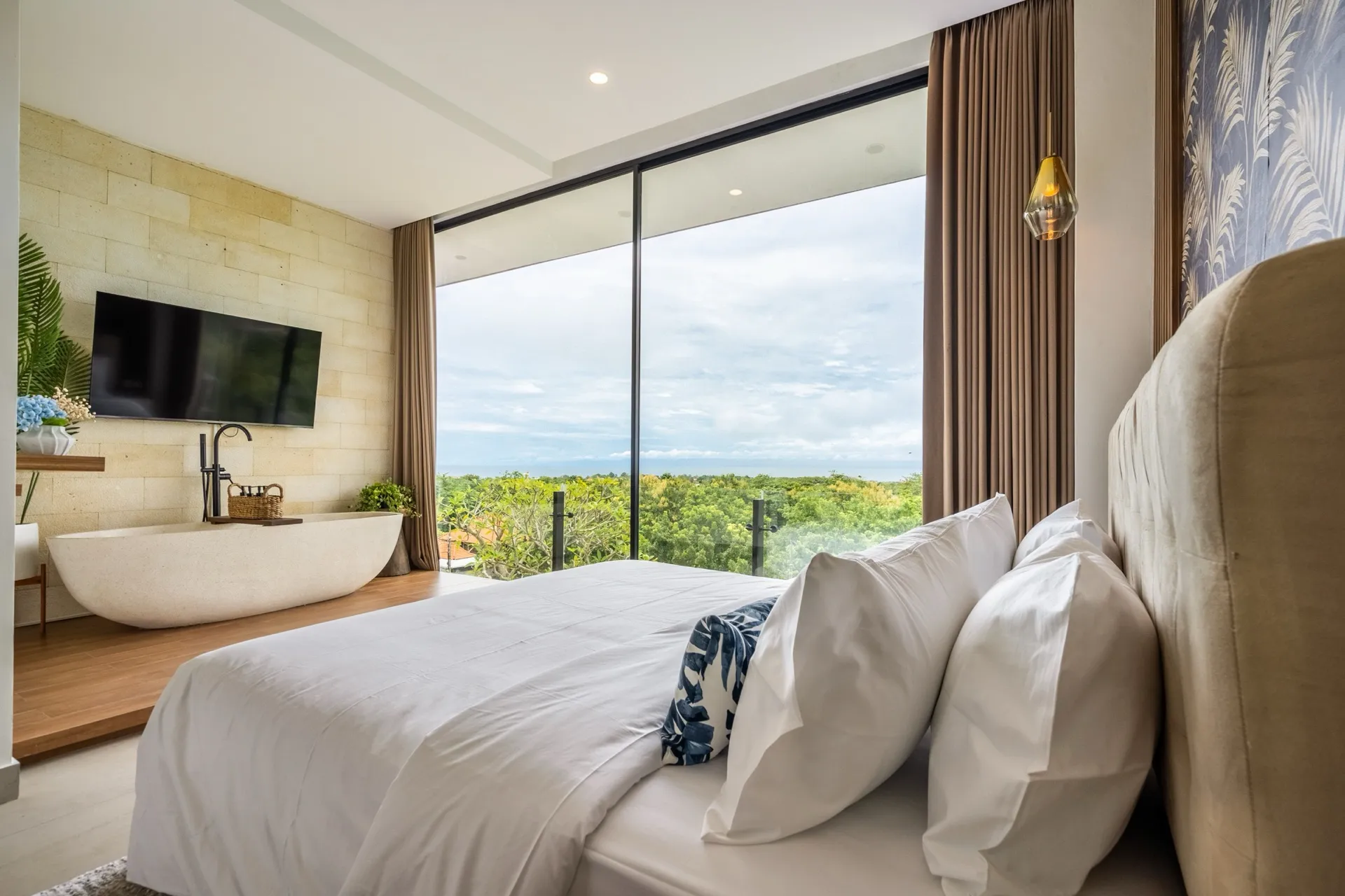 A bedroom suite at Villa Pepper with a freestanding stone bath and full-height glass facing the treetops and the sea